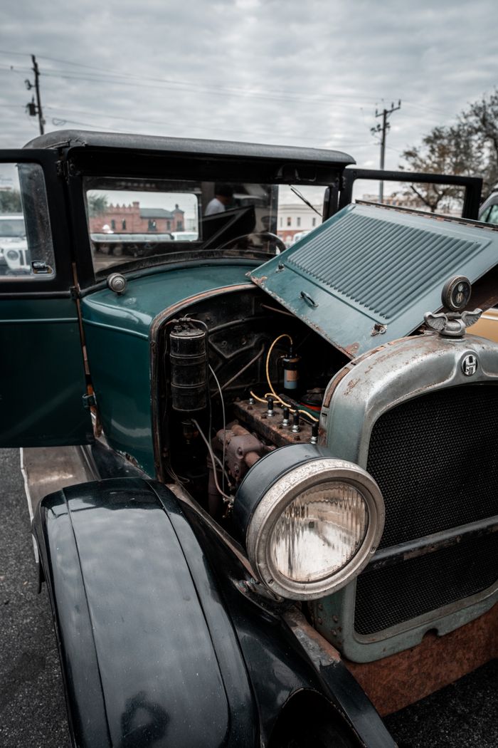 Old-fashioned green car with an open hood showcasing its engine in a city setting.